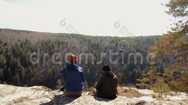 游客夫妇坐在岩石上看针叶林。 日落时分远离家乡的冒险
